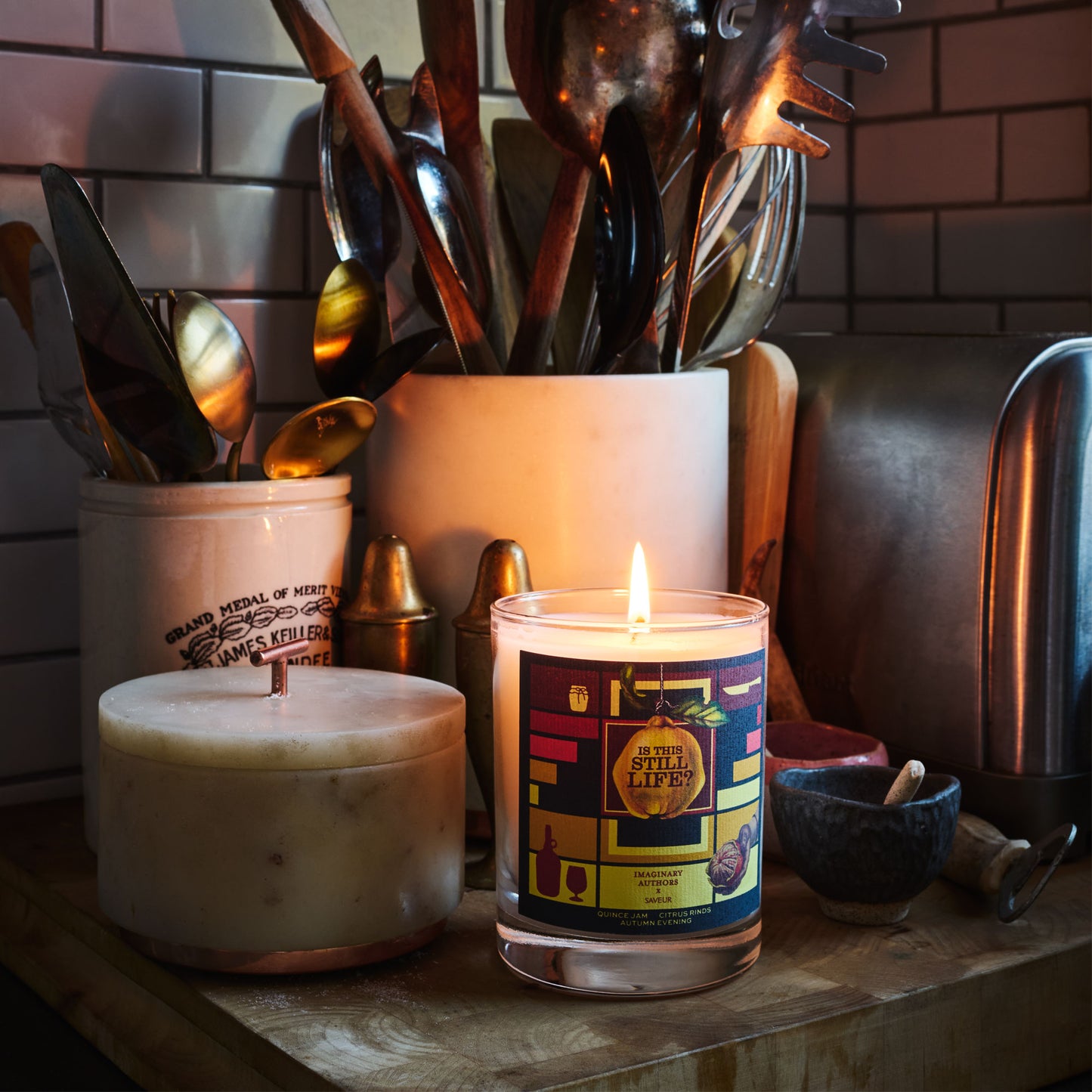 Imaginary Authors X SAVEUR “Is This Still Life?” Candle on a kitchen counter with utensils, a salt pig, and a bread box in the background